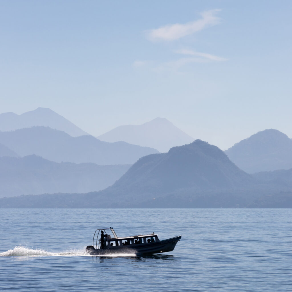 Boot auf dem Lago de Atitlán, im Hintergrund Vulkangipfel